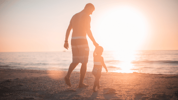 Man walking child on the beach at sunset